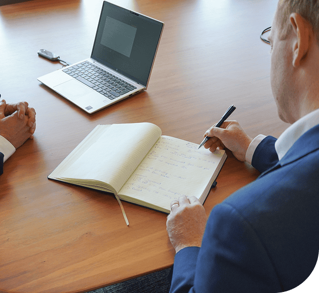 Professional business meeting with handwritten notes and a laptop on a wooden table, representing corporate consulting, strategic planning, and professional services at RQC Group.